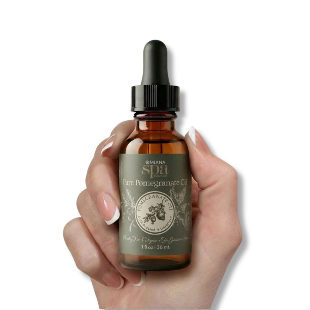 Hand holding a bottle of 'Omiana Spa Pure Pomegranate Oil' with a dropper on a white background